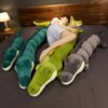 Une jeune femme dort sur un lit avec trois grands coussins en forme de crocodile. Deux sont verts et un est gris.