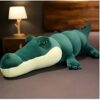 Une grande peluche en forme de crocodile vert sur un lit.