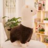 Une peluche de lama blanche avec un manteau brun, debout sur une table blanche.