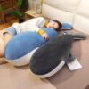 Une femme dort sur un lit avec deux gros coussins en forme de baleine, l'un bleu et l'autre noir.