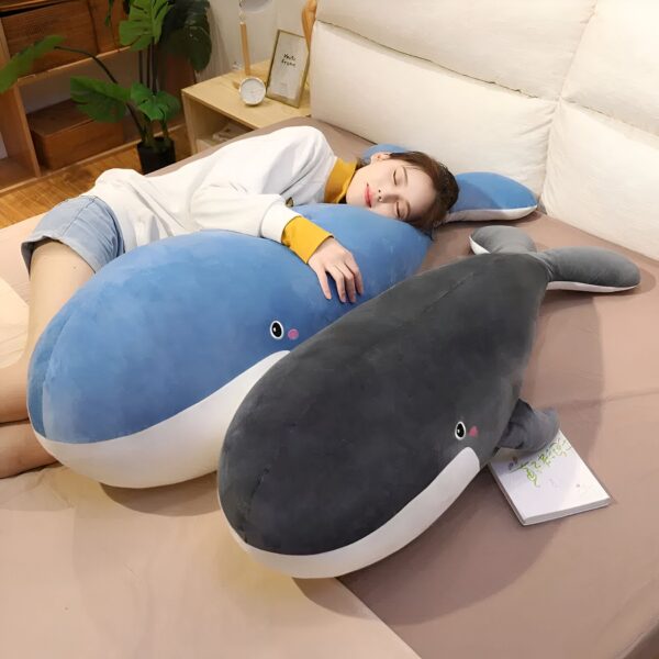 Une femme dort sur un lit avec deux gros coussins en forme de baleine, l'un bleu et l'autre noir.