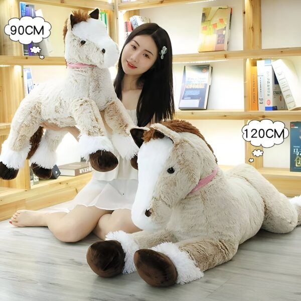 grande-peluche-cheval-marron-90cm-peluche-geante-pour-canape-2a Une jeune femme tient une grande peluche de cheval beige avec des détails blancs et bruns. Sur le sol, on trouve un autre cheval en peluche, encore plus grand, de la même couleur. Les deux peluches mesurent 90 cm et 120 cm.