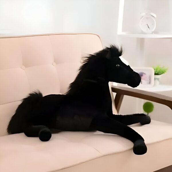 Une peluche noire en forme de cheval couché sur un canapé beige.