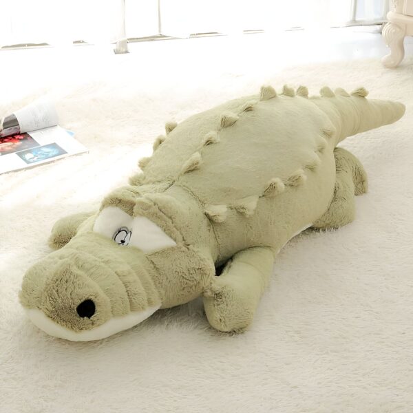 Grande peluche crocodile vert allongé sur un tapis blanc.