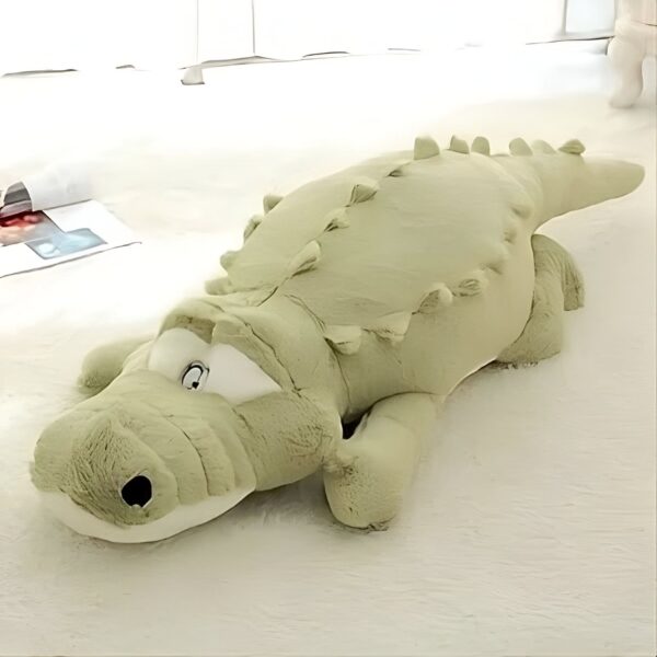 Grande peluche de crocodile vert allongé sur un fond blanc.