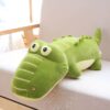 Un grand crocodile en peluche vert avec des yeux noirs et une bouche cousue sur un canapé beige.