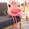 Une peluche rose en forme de flamant rose assis sur un canapé en bois.