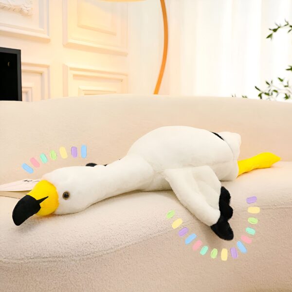 grande-peluche-flamant-rose-geante-130cm-160cm-190cm-10a-3 Une peluche de flamant rose blanc et jaune allongée sur un canapé beige.