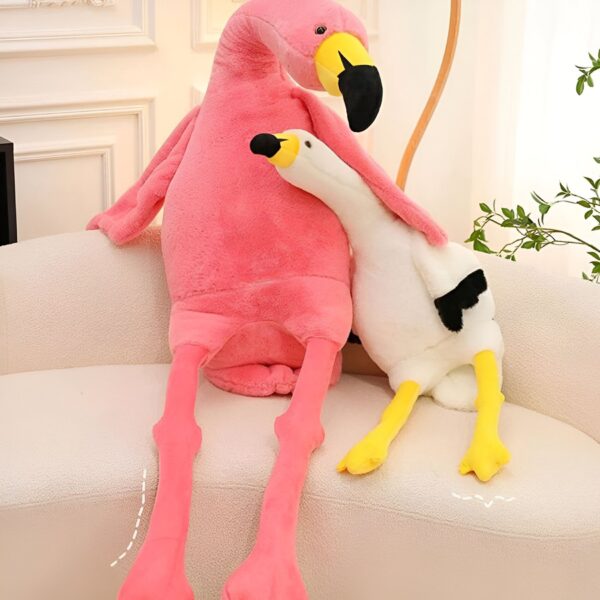 Deux peluches en forme de flamant rose et d'oie blanche, assises sur un canapé blanc.