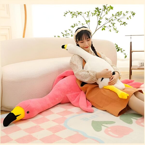 grande-peluche-flamant-rose-geante-130cm-160cm-190cm-3a-1 Une femme assise sur un canapé avec un grand coussin en forme de flamant rose et un oreiller en forme d'oie.