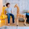 Un jeune garçon souriant assis sur un fauteuil jaune avec une grande girafe en peluche à côté de lui.