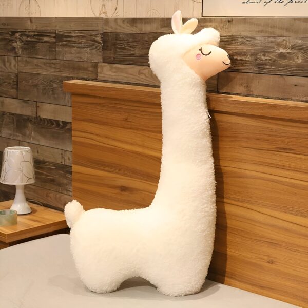 grande-peluche-lama-geante-cadeau-ideal-pour-enfants-et-adultes-6a-2 Un oreiller en forme de lama blanc moelleux posé sur un lit avec une tête de lit en bois.