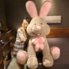 Une jeune femme sourit en tenant un grand lapin en peluche marron avec un nœud rose.