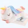 Une peluche de licorne blanche avec une crinière arc-en-ciel et une queue rose, allongée sur le dos, les yeux fermés, avec des étoiles sur le dos.