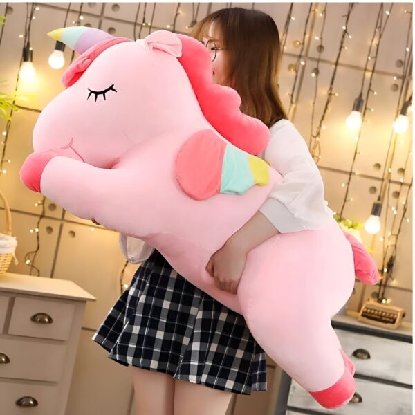 Une jeune femme tenant une grande peluche rose en forme de licorne avec une crinière et une queue arc-en-ciel.