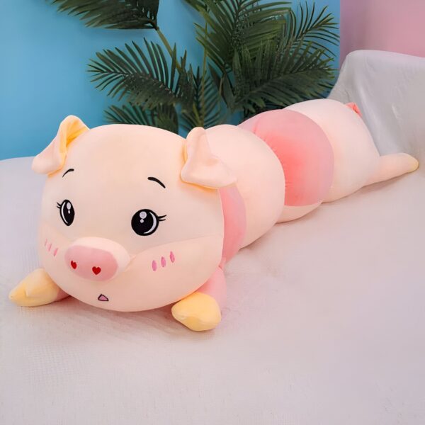 Gros coussin en forme de cochon rose avec des yeux noirs et une petite bouche. Il est posé sur un lit blanc.