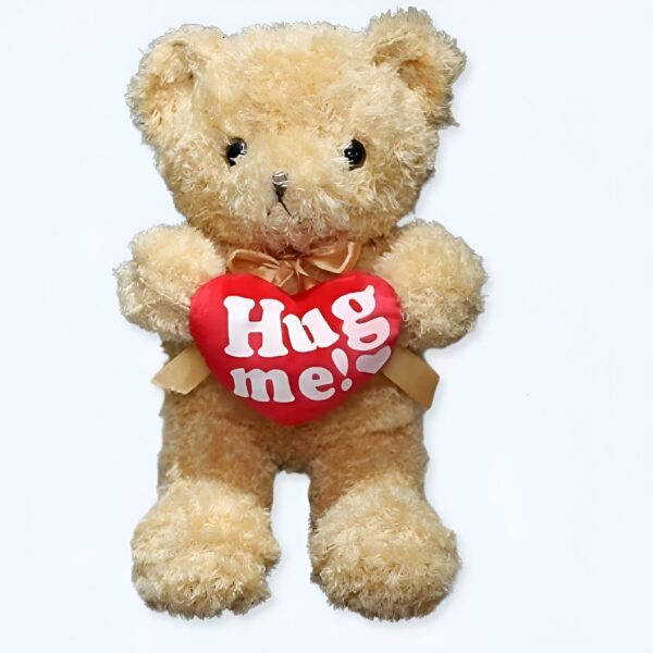 Ours en peluche beige tenant un cœur rouge avec l'inscription "Hug me !" en lettres blanches.