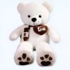 Un grand ours en peluche blanc portant un foulard brun avec un cœur brun sur lequel est inscrit "Love". Les pattes de l'ours sont également brunes et ornées de cœurs.