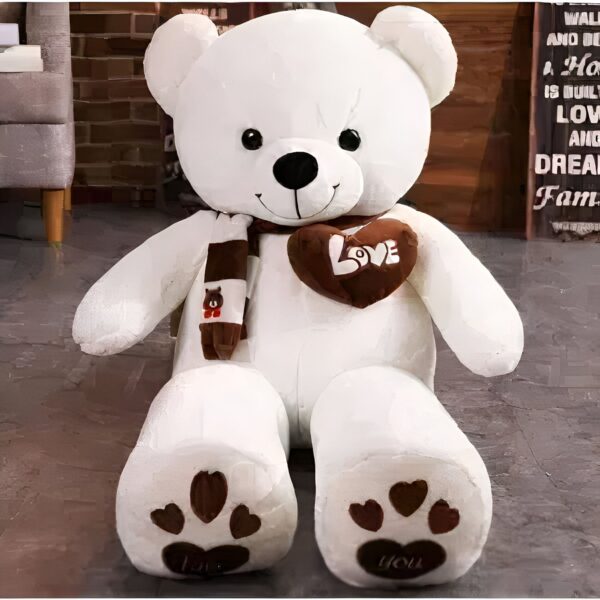 Un gros ours en peluche blanc avec une écharpe marron et un cœur marron avec le mot "love" écrit dessus. Il a des coussinets bruns sur les pieds.