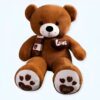 Un grand ours en peluche brun portant un foulard et un cœur avec l'inscription "Love" sur la poitrine. Les pattes de l'ours ont des empreintes de pattes avec l'inscription "Love you".