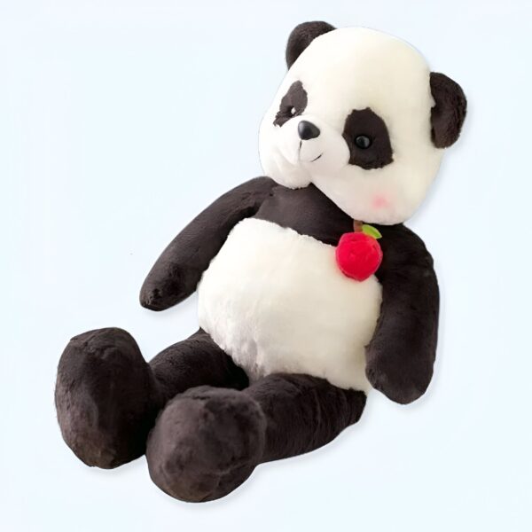 Une peluche de panda noir et blanc avec un noeud rouge en forme de pomme sur son ventre, assis sur un fond blanc.