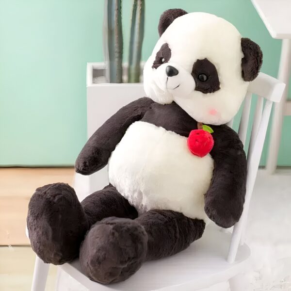 grande-peluche-panda-geante-a-caliner-peluche-panda-douce-et-molle-2a Grande peluche panda noir et blanc assis sur une chaise blanche avec une pomme rouge.