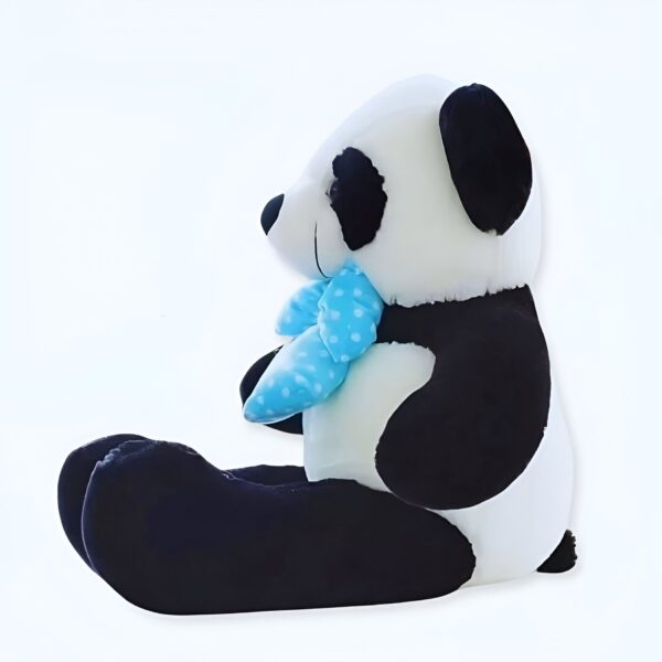 Une grande peluche panda noire et blanche assise avec un noeud bleu à pois.