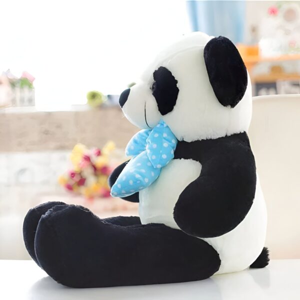 Une peluche panda noire et blanche assise avec un nœud bleu à pois blancs.