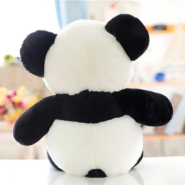 Une peluche en forme de panda noir et blanc assise sur une surface blanche.