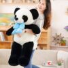 Une jeune femme souriante tenant une grande peluche panda avec un nœud bleu à pois blancs.