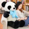 Une jeune femme assise sur un canapé avec un grand ourson en peluche panda portant un nœud papillon bleu.