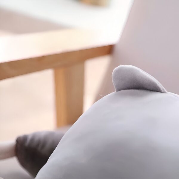 Une partie d'un coussin gris en forme d'animal assis sur un fauteuil en bois.