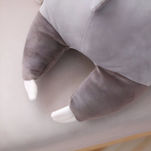 Gros plan sur les pattes de la peluche en forme de paresseux, montrant les détails de la fourrure grise et des griffes blanches.