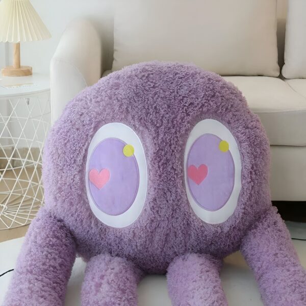 Un gros coussin violet en peluche avec de grands yeux et un cœur rose brodé.