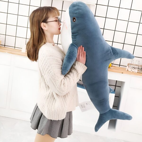 Une jeune femme tenant un grand requin en peluche bleu et blanc.