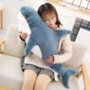 Une femme est assise sur un canapé avec une grande peluche en forme de requin bleu dans ses bras.
