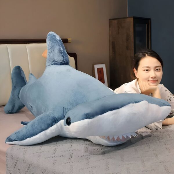 Une femme sourit en posant la tête sur un grand requin-marteau en peluche bleu.