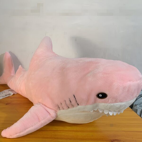 Grande peluche de requin rose sur un fond en bois.