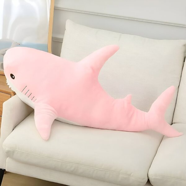 Un grand requin rose en peluche couché sur un canapé blanc.