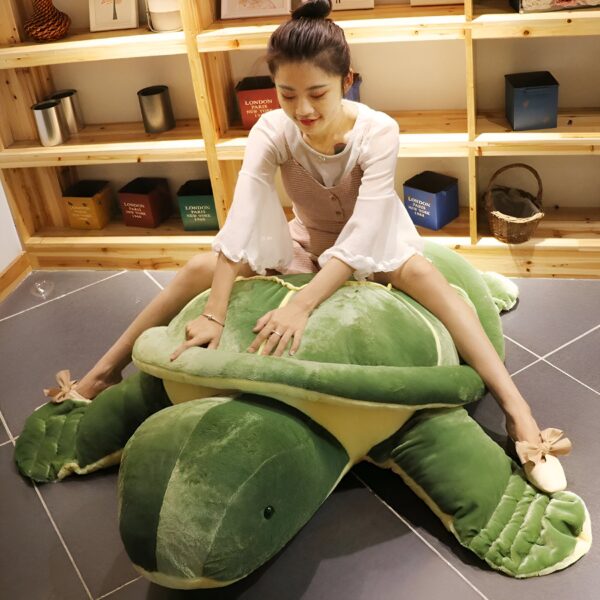 Une jeune femme assise sur une grande peluche en forme de tortue verte. La tortue est très réaliste et a des détails précis. La femme a l'air heureuse et détendue.