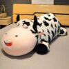 grande-peluche-vache-pour-dormir-doudou-confort-et-tranquillite-1a Une grande peluche vache noire et blanche allongée sur un lit, avec un sourire et des yeux fermés.