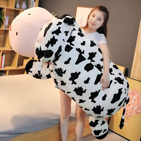 grande-peluche-vache-pour-dormir-doudou-confort-et-tranquillite-3a Une femme tenant un gros coussin en forme de vache à motifs noirs et blancs.