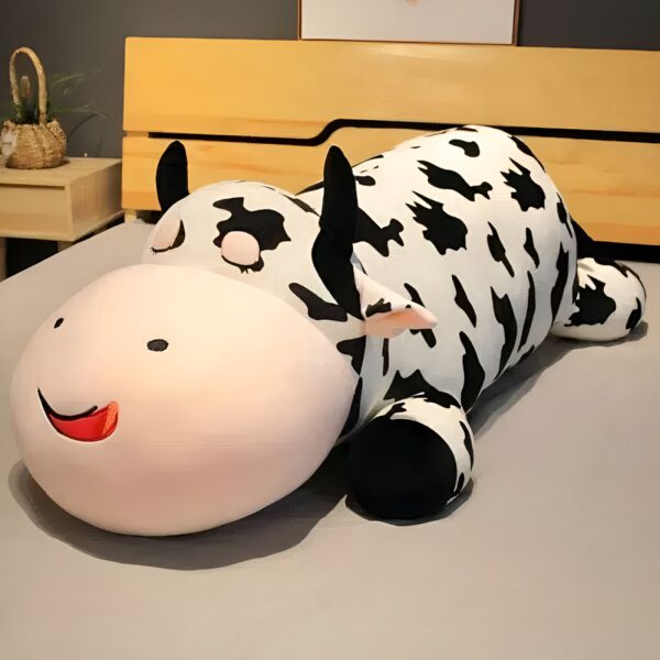 grande-peluche-vache-pour-dormir-doudou-confort-et-tranquillite-4a Grande peluche vache noire et blanche couchée sur un lit avec un sourire.