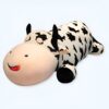 grande-peluche-vache-pour-dormir-doudou-confort-et-tranquillite-5a-1 Une peluche en forme de vache noire et blanche couchée sur le dos avec les yeux fermés et un sourire.