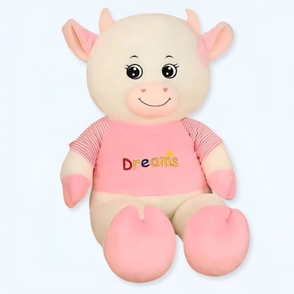 Grande peluche de vache blanche avec un t-shirt rose portant le mot "Dreams" en lettres colorées.