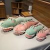 grosse-peluche-crocodile-verte-jouet-doux-pour-bebe-et-enfant-differentes-tailles-3a Quatre crocodiles en peluche en vert, rose et beige posés sur un lit blanc.