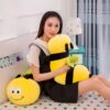 peluche-abeille-coussin-souriante-jouet-en-peluche-doux-pour-enfants-3a-2 Une jeune femme assise sur un lit avec deux coussins en forme d'abeille.