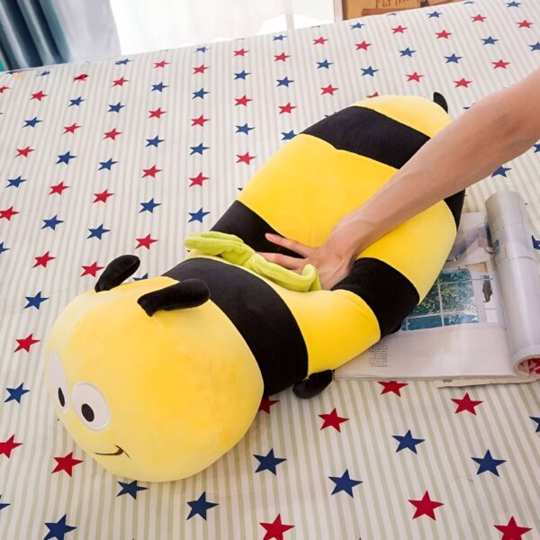 peluche-abeille-coussin-souriante-jouet-en-peluche-doux-pour-enfants-4a-2 Un gros coussin en forme d'abeille jaune et noire sur un lit avec des étoiles rouges et bleues.