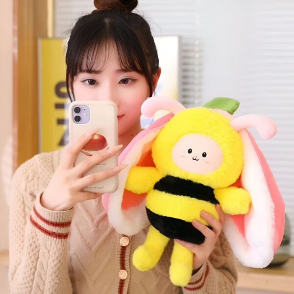Une jeune femme tenant une peluche abeille jaune et noire avec des ailes de papillon roses et blanches.