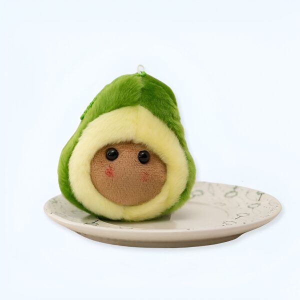 Peluche avocat souriant avec de gros yeux noirs sur une assiette blanche.